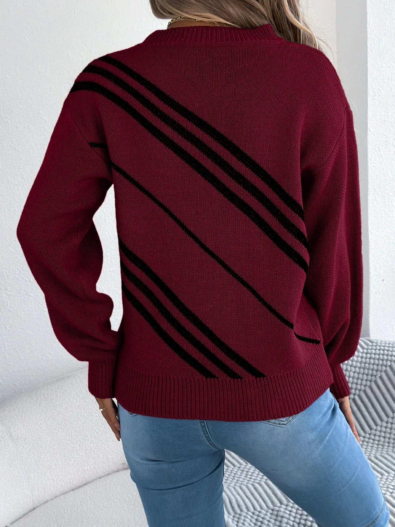 Back view of a woman wearing a maroon knit sweater with black diagonal stripes.