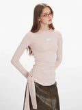 Close-up of a woman wearing a light pink long-sleeve ruched top with a tie detail