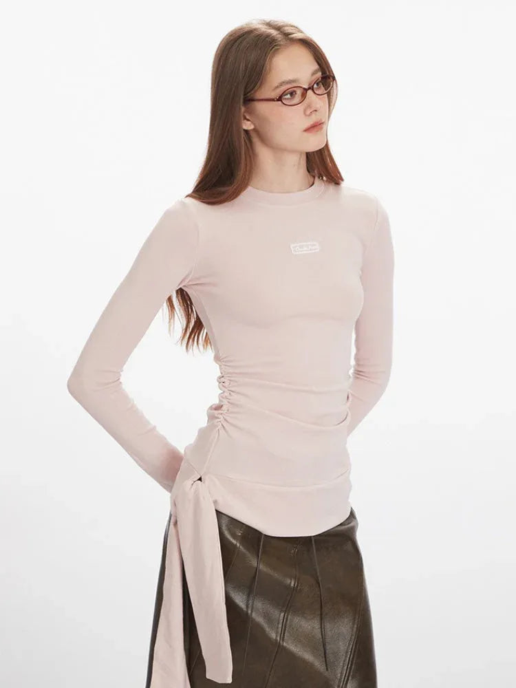 Close-up of a woman wearing a light pink long-sleeve ruched top with a tie detail