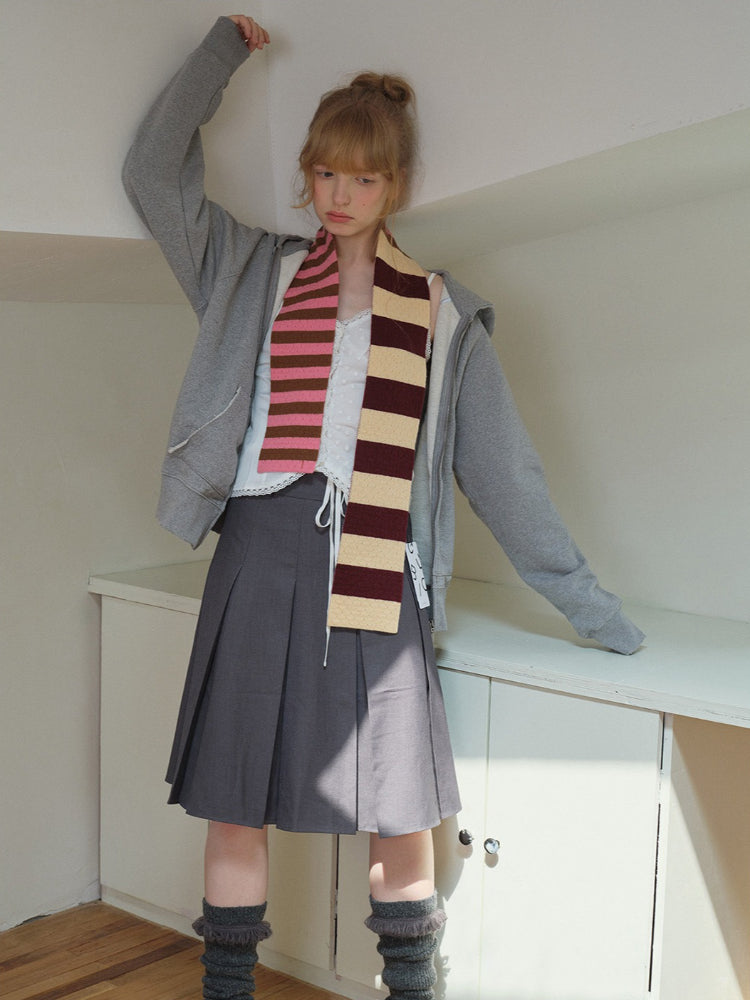 Model striking a pose with arms raised, wearing a gray zip-up hoodie, a gray pleated skirt, and a striped scarf.