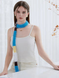 Close-up of a woman wearing a white ribbed tank top and cream pants, with a colorful fuzzy knit scarf draped around her neck.