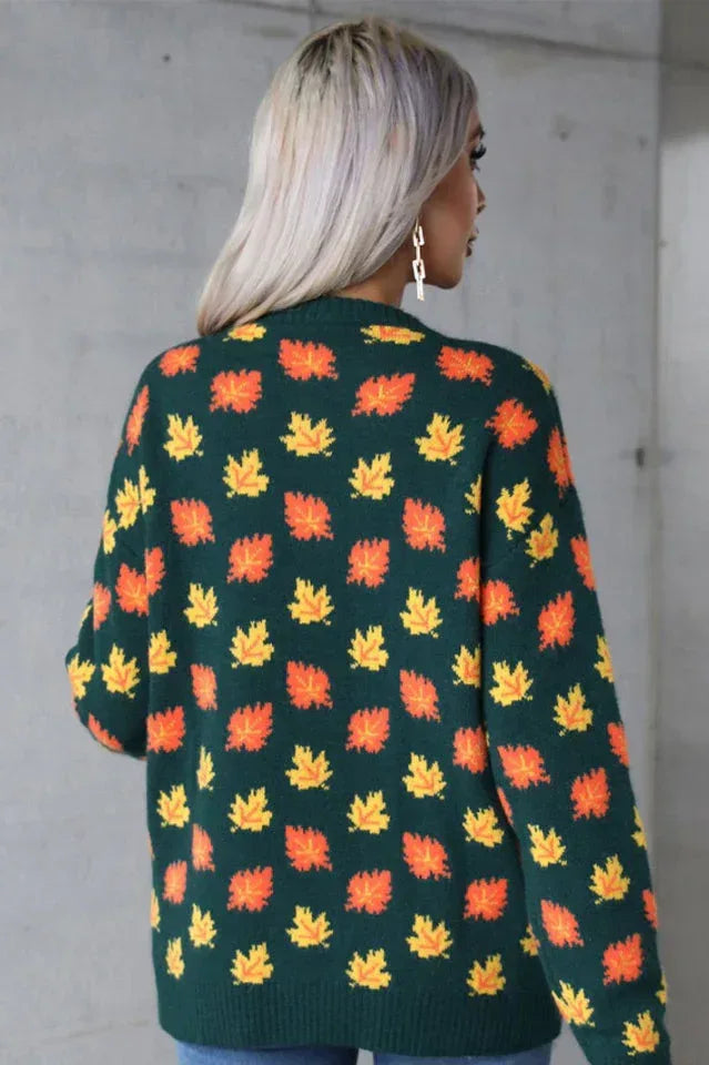 Back view of a woman wearing a dark green knit sweater with an orange and yellow leaf print.