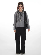 Woman wearing a grey crew neck sweater with black cargo pants and a striped scarf