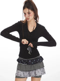 Close-up front view of a woman wearing a black long-sleeve top and layered skirt, holding a necklace with a heart pendant