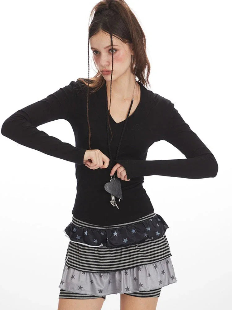 Close-up front view of a woman wearing a black long-sleeve top and layered skirt, holding a necklace with a heart pendant