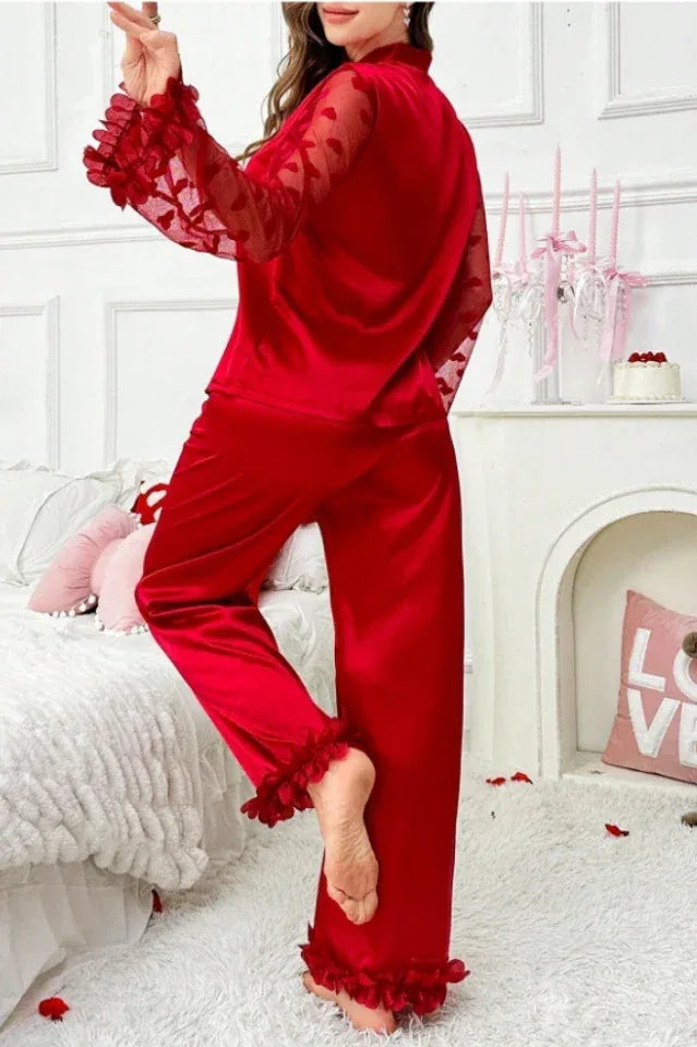 Rear view of a woman in a red satin pajama set featuring sheer heart-patterned sleeves and ruffled accents