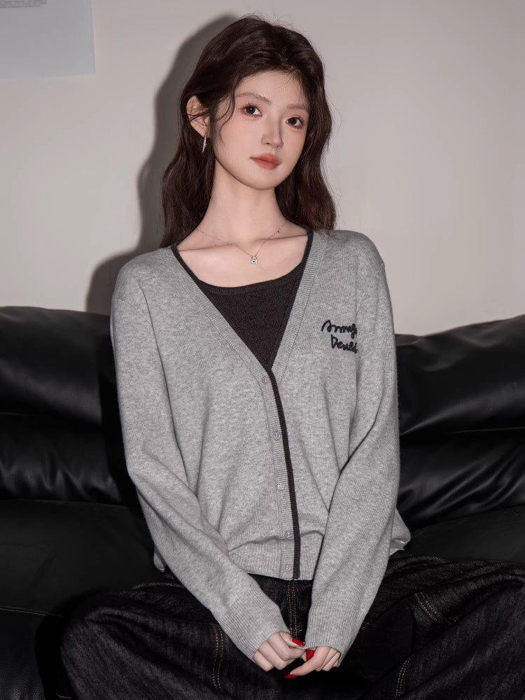Woman wearing a grey V-neck knit cardigan with contrast trim and embroidered graphic detail
