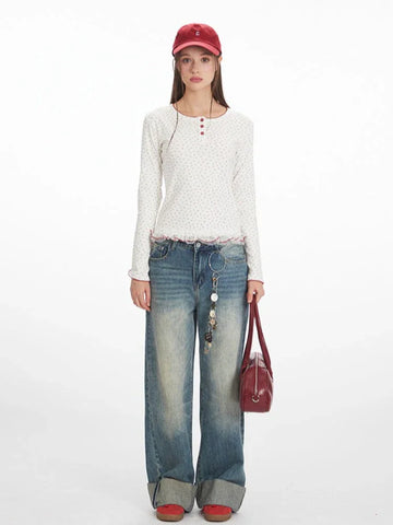 Woman wearing a white long-sleeve top with a red floral print and red trim, paired with distressed denim jeans.