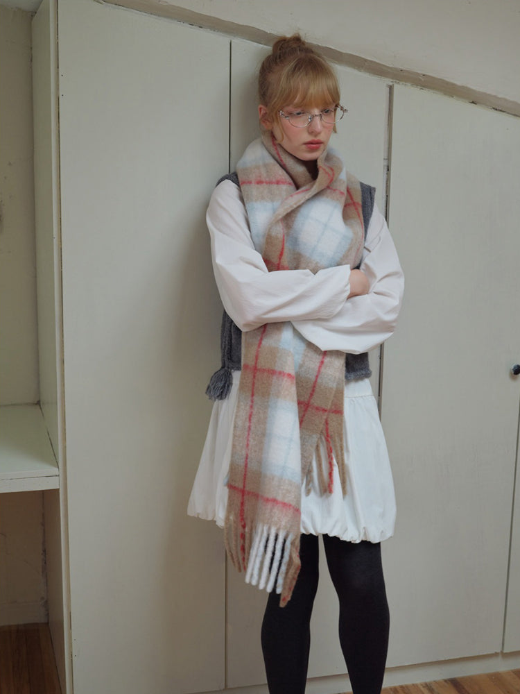 Model wearing a large plaid scarf with fringe trim over a white shirt and dark leggings.