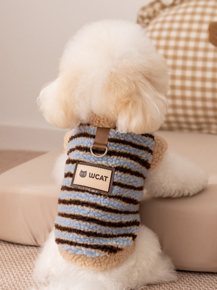 Back view of a small white dog in a striped fleece vest with a leash ring