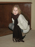 Woman wearing a light grey crewneck sweatshirt, dark grey leggings, and a dark brown fringed scarf.