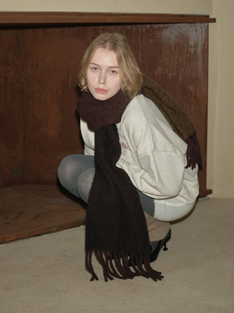 Woman wearing a light grey crewneck sweatshirt, dark grey leggings, and a dark brown fringed scarf.