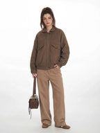 Woman holding a brown handbag while wearing a brown textured bomber jacket and tan wide-leg pants.