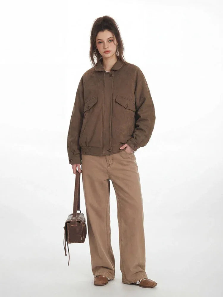 Woman holding a brown handbag while wearing a brown textured bomber jacket and tan wide-leg pants.