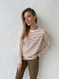Woman wearing a white and brown striped long sleeve top and brown pants.