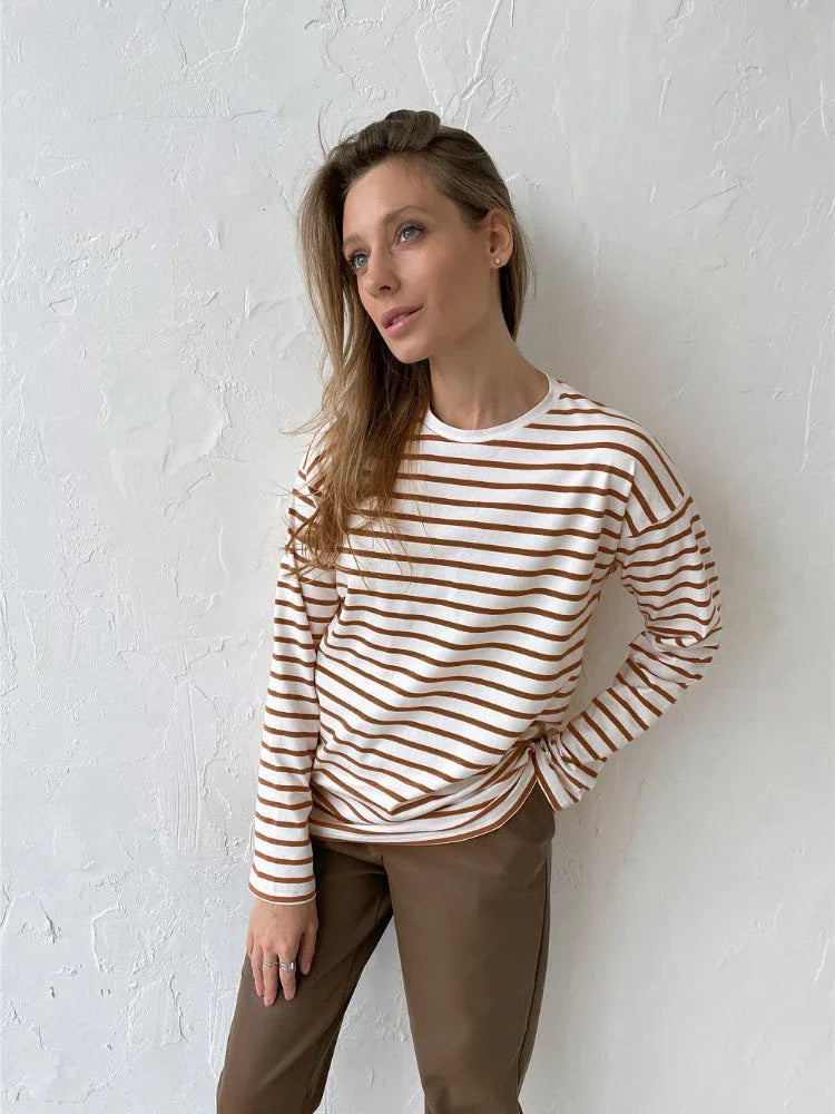 Woman wearing a white and brown striped long sleeve top and brown pants.