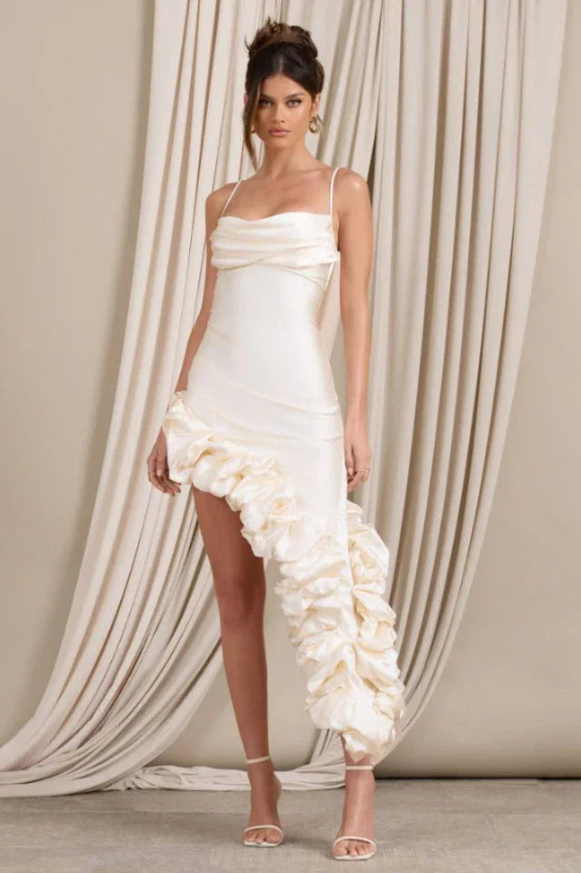Woman wearing a cream satin bodycon dress with spaghetti straps, a ruched sweetheart neckline, and an asymmetrical ruffled high-low hemline.