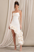 Woman wearing a cream satin bodycon dress with spaghetti straps, a ruched sweetheart neckline, and an asymmetrical ruffled high-low hemline.