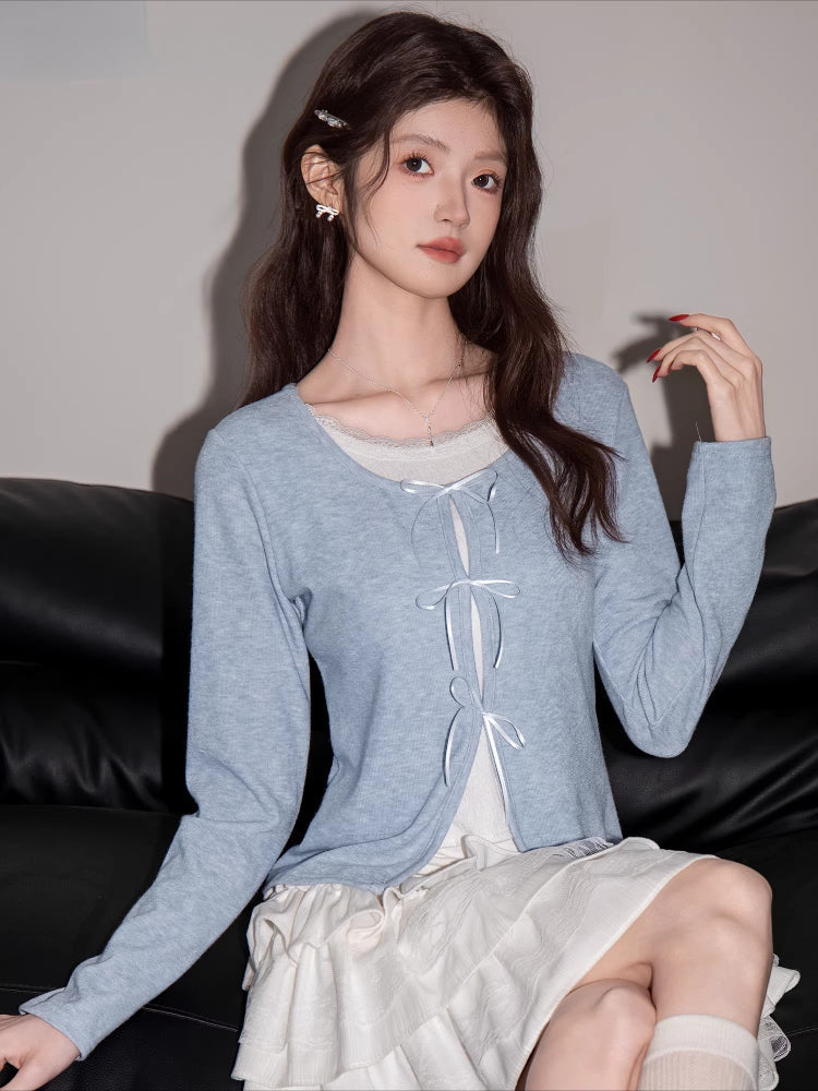 Woman sitting on a black sofa wearing a light blue knit cardigan and white tiered skirt.