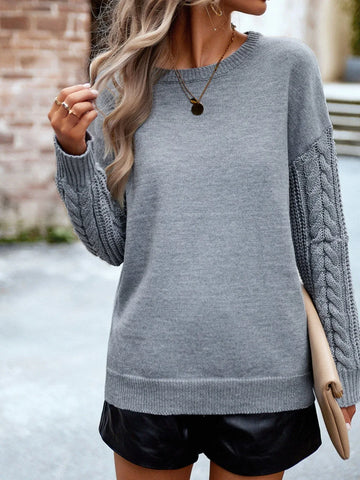 Woman wearing a grey crew neck knit sweater with cable knit sleeves and black shorts