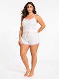 Woman wearing a white ribbed camisole and shorts pajama set with pink lace trim and bow details, side view, right.