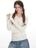 Woman in a white ribbed knit long-sleeve top with a collared button-up neckline and a detachable hood, showing off the sleeve detail and necklace.