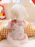 Back view of a white dog wearing a pink and white traditional Chinese style dog jacket with floral embroidery and pink faux fur trim.