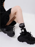 A person wearing black crew socks with a cartoon cat applique, sitting down with black chunky shoes.