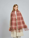 Full shot of a woman modeling a large plaid scarf in pink and beige tones.