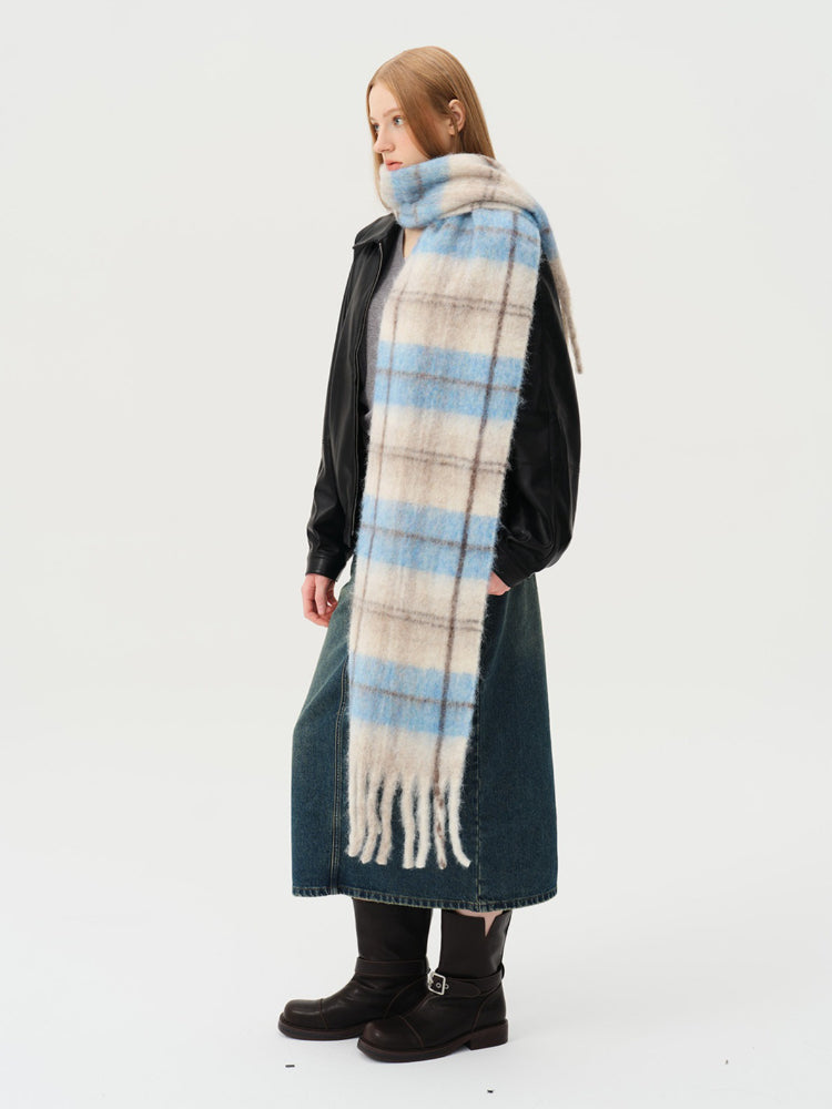 Woman wearing a plaid scarf with blue and beige squares and a fringed hem, paired with a black jacket and denim skirt.