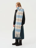 Side view of a woman wearing a plaid scarf with blue and beige squares and a fringed hem.