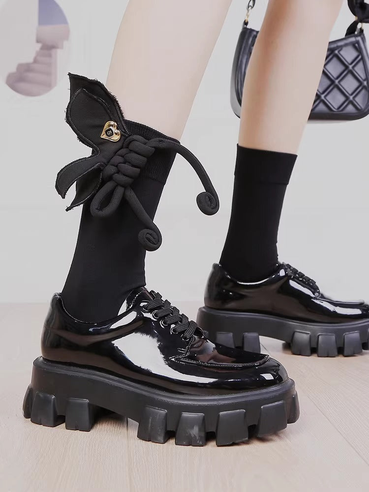 Close-up of black mid-calf socks with a 3D rope bow and gold heart charm.