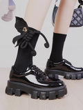 Close-up of black mid-calf socks with a 3D rope bow and gold heart charm.