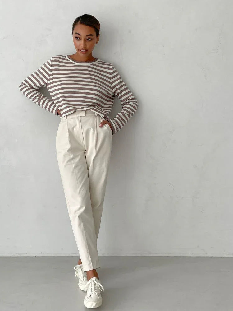 Full-body shot of a woman wearing a striped long-sleeve top and cream trousers, with hands on hips.