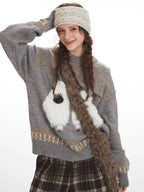 Woman posing playfully while wearing a grey knit sweater with a graphic sheep print and plaid wide leg pants.