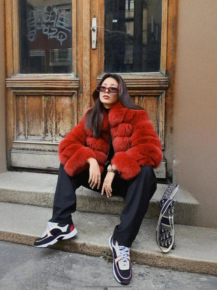 Woman wearing a red faux fur cropped jacket, black pants, and sneakers, sitting on steps.