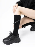 Person wearing black knee-high socks with stud accents and a strap, in a seated pose with chunky sneakers.