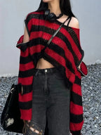 Woman wearing a red and black striped knit sweater with cut-out details and zippered sleeves, paired with dark wash jeans.