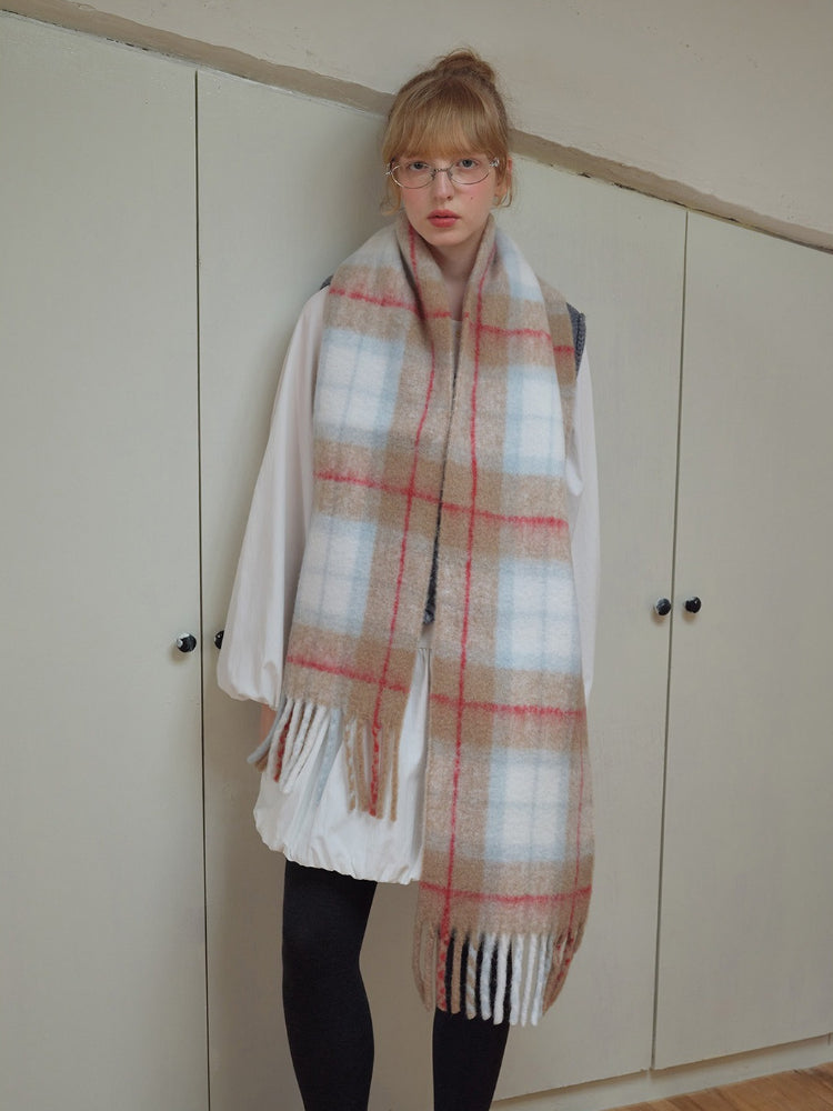 Model wearing a large plaid scarf with fringe trim over a white shirt and dark leggings.