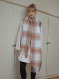 Model wearing a large plaid scarf with fringe trim over a white shirt and dark leggings.