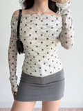 Close-up of a woman's torso wearing a polka dot sheer mesh top with an off-the-shoulder neckline.