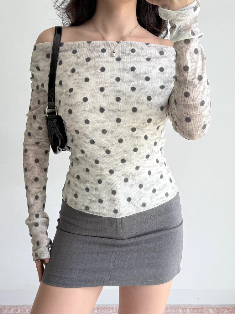 Close-up of a woman's torso wearing a polka dot sheer mesh top with an off-the-shoulder neckline.