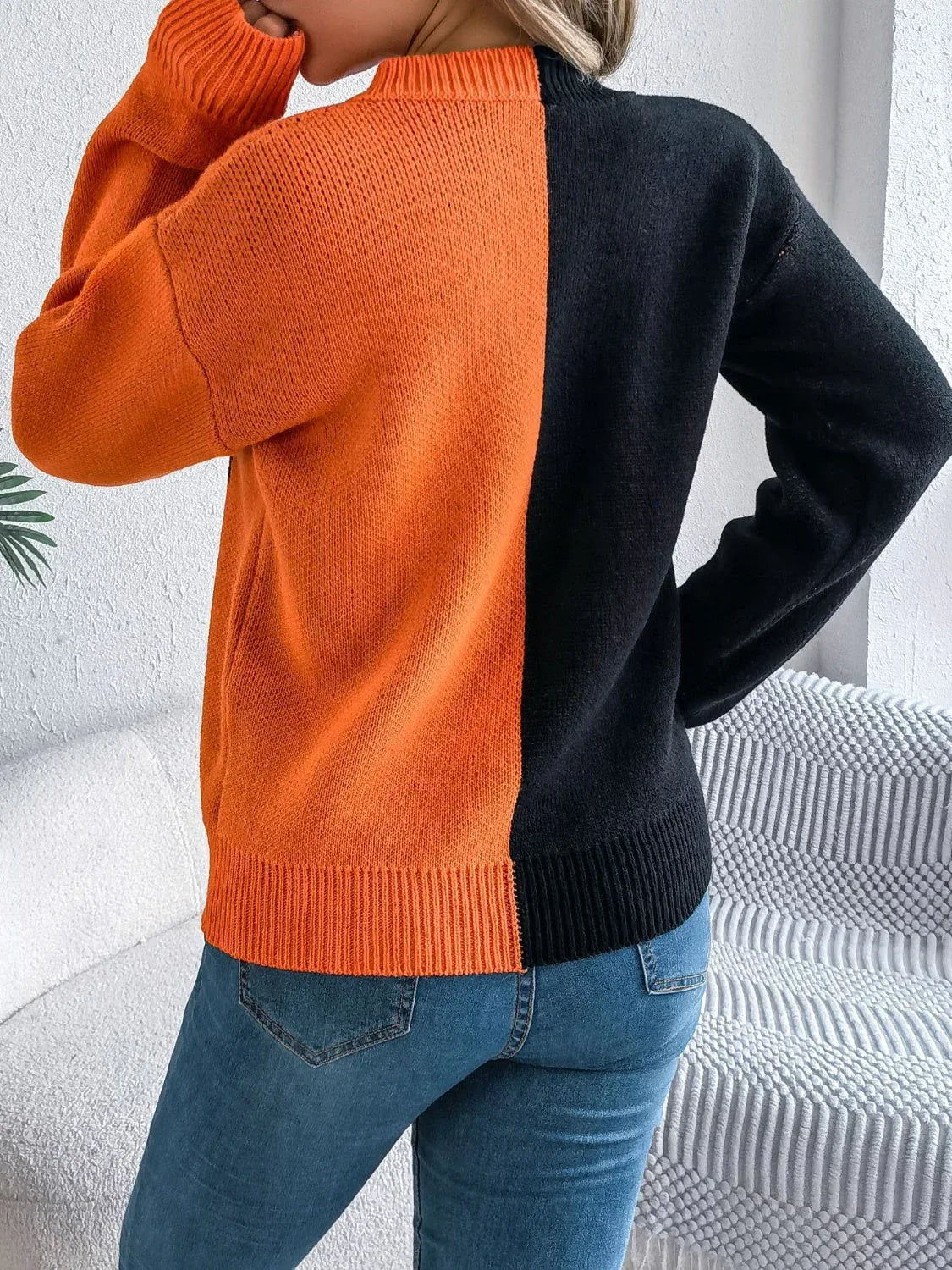 Back view of a woman wearing a black and orange two-tone knitted sweater.