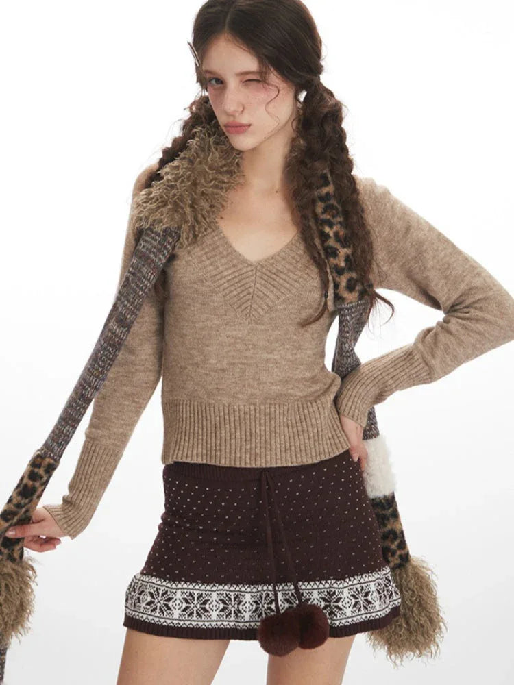 Close-up of a woman wearing a beige V-neck knit sweater and brown patterned skirt, with a patterned scarf draped around her neck.