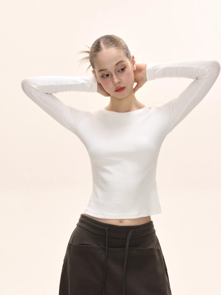Woman adjusting her hair, showcasing the white long-sleeve fitted top.