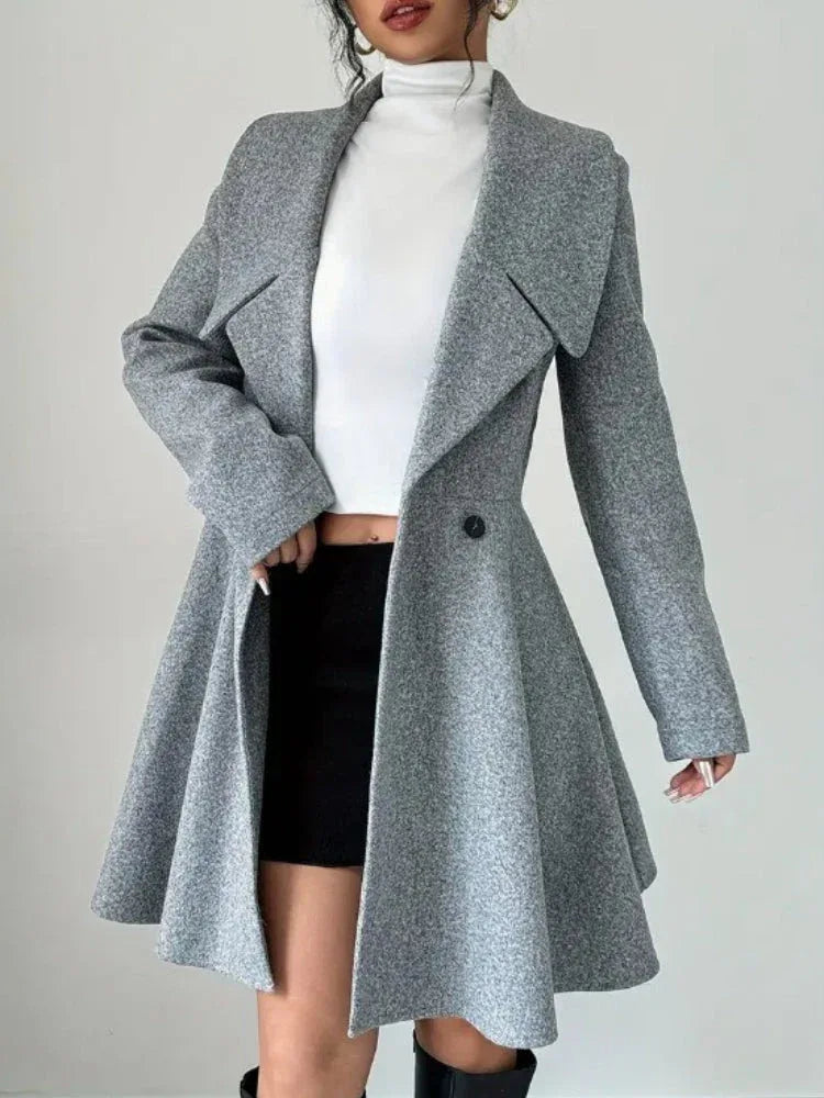 Woman wearing a grey fit-and-flare coat over a white turtleneck and black skirt.
