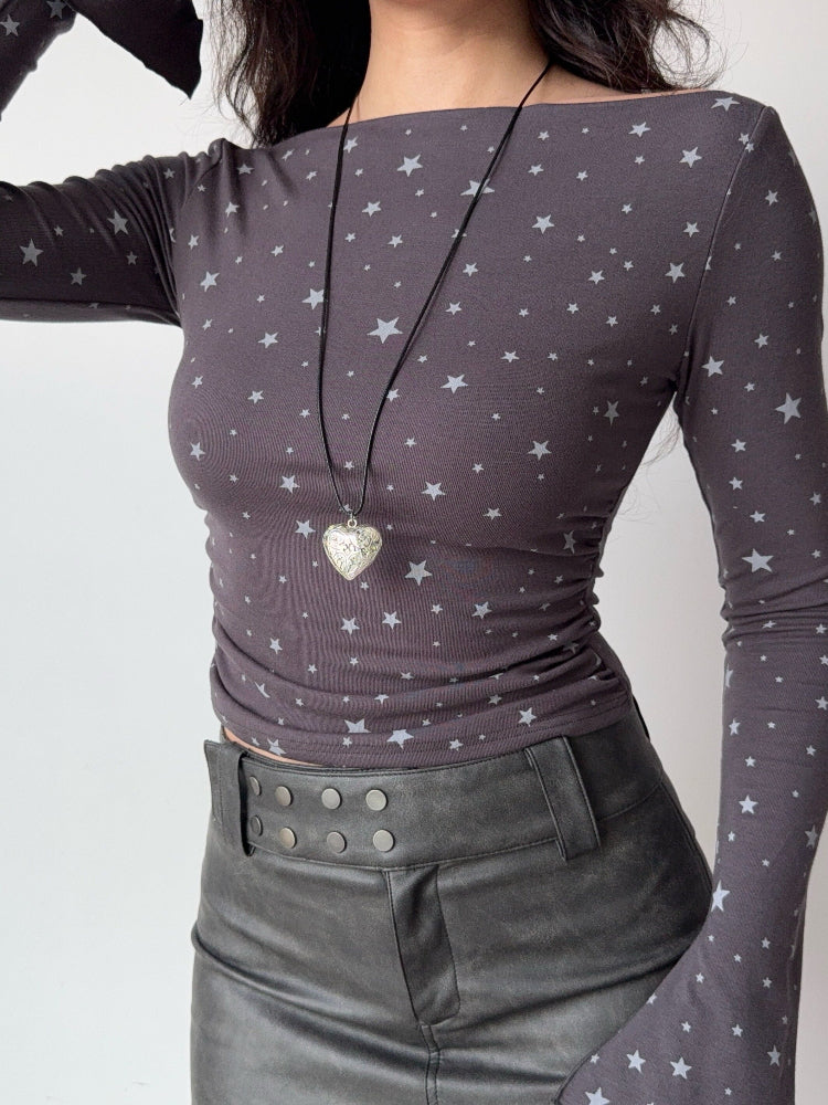 Woman wearing a grey long-sleeve top with a white star print and a heart pendant necklace.