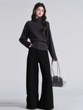 Full body shot of a woman in a dark grey knit sweater and black trousers