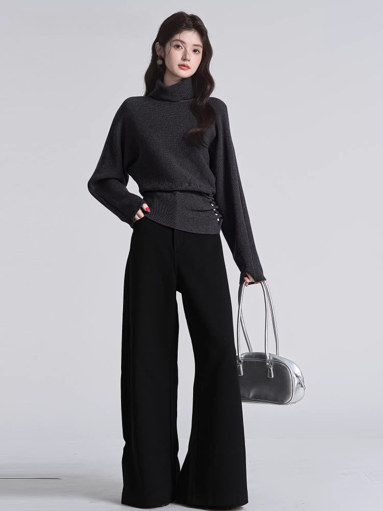 Full body shot of a woman in a dark grey knit sweater and black trousers