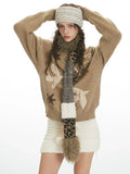Close-up of a woman wearing a tan intarsia knit sweater with birds and stars, a white textured mini skirt, and a patterned scarf.